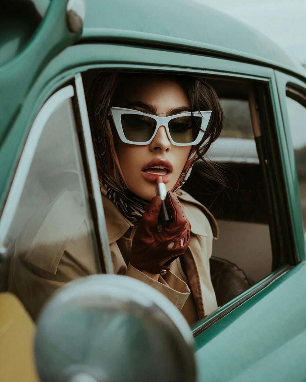 Actrice à grandes lunettes blanches, foulard et trench, au volant d'une décapotable vert pastel